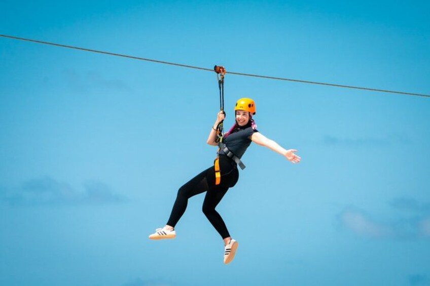 A person zip-lining with a harness and helmet, suspended in mid-air against a clear blue sky. 2