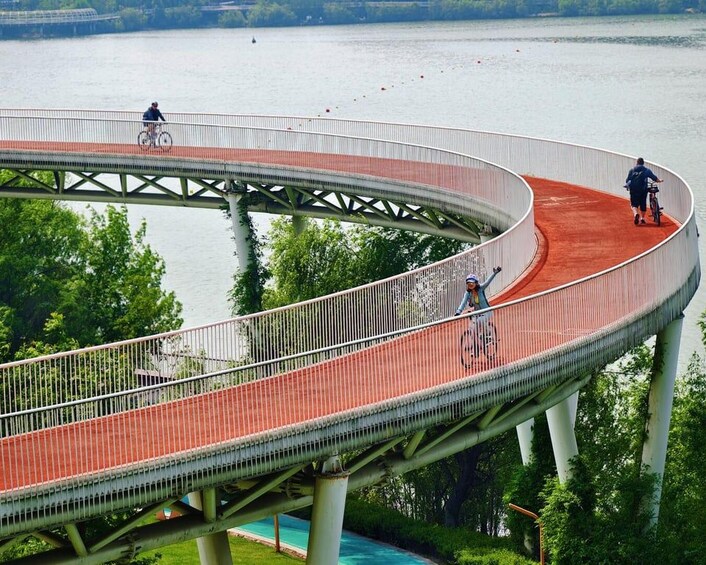 En buet fodgængerbro over vand med cyklister på. 5