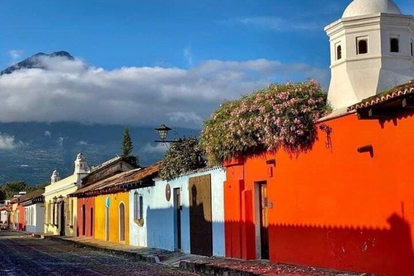 A colorful street with buildings, a white tower, and a mountain in the background. 2