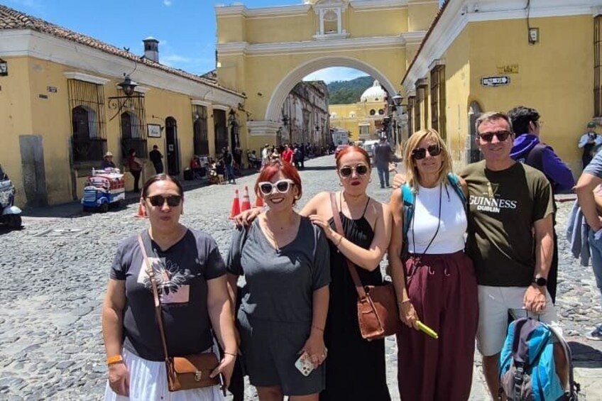 A group of people standing on a cobblestone street with yellow buildings and a large archway in the background. 3