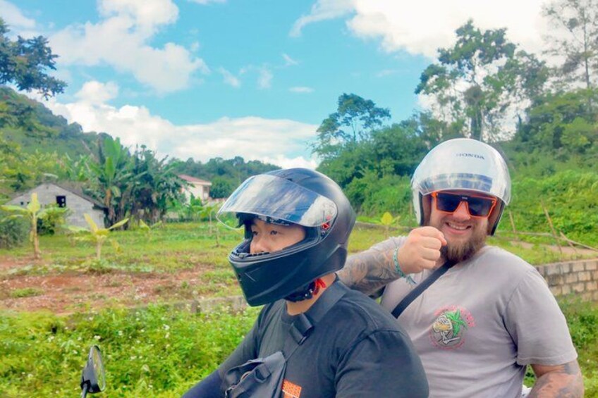 Two people wearing helmets, one with a Honda logo, in a rural setting with greenery and a clear sky. 2