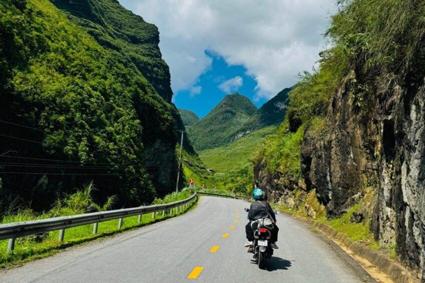A motorcycle on a winding mountain road with lush greenery and rocky cliffs. 4