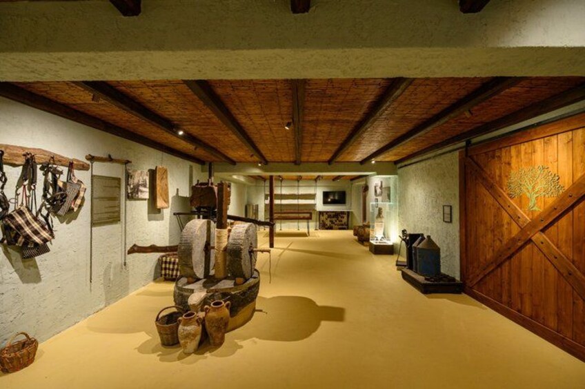 A rustic interior with wooden beams, a large wooden door with a tree design, and various historical artifacts displayed on the walls and floor. 3