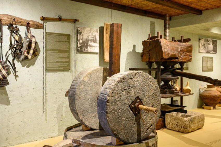 A historical exhibit with stone millstones, wooden tools, and a traditional press. 4