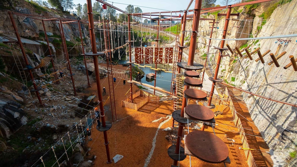 An outdoor adventure park with rope bridges, wooden platforms, and a rocky terrain. 2