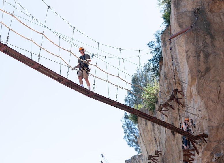 A person navigating a rope bridge over a rocky terrain. 3