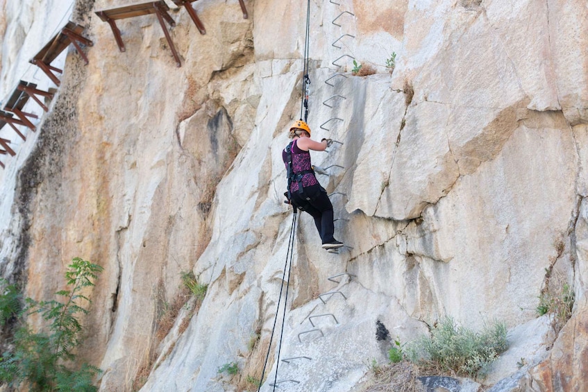 A person rock climbing on a large rock face with metal anchors. 4