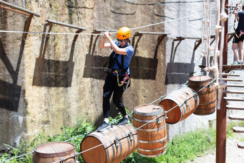 A person navigating an obstacle course with wooden barrels and ropes. 1