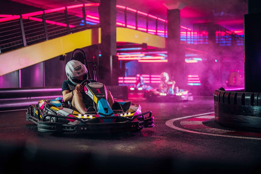 A go-kart racer in a colorful go-kart on a track with neon lights in the background. 4