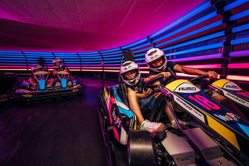 Go-karts with drivers in a brightly lit indoor track. 1