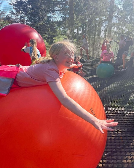 A child on a large orange ball in a netted area with trees in the background. 1