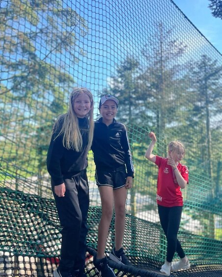 Three individuals on a netted climbing structure with trees in the background. 3