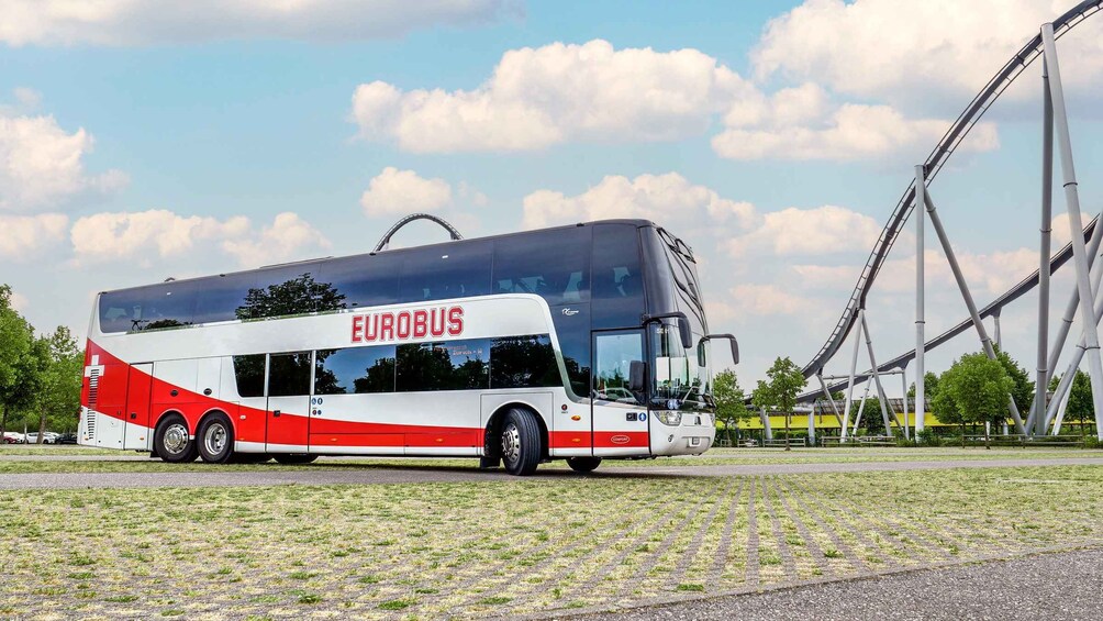 A Eurobus with a red and white design parked on a grassy area with a roller coaster in the background. 1