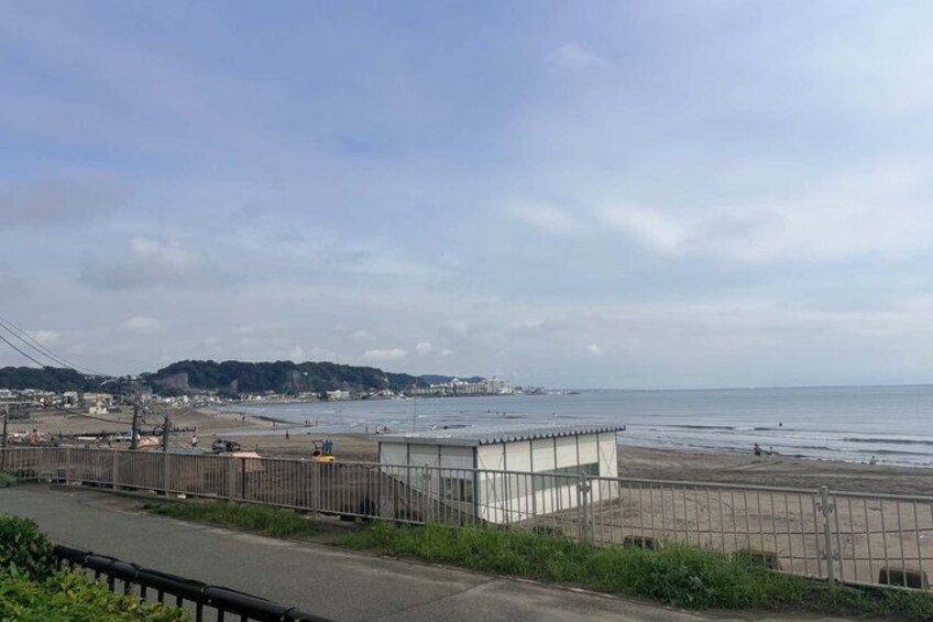 A coastal road with a beach, a small building, and distant hills. 1
