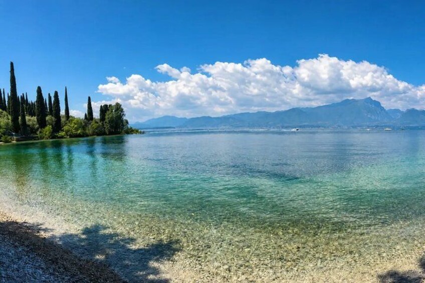 A clear lake with a rocky shore, trees, and mountains in the distance. 5
