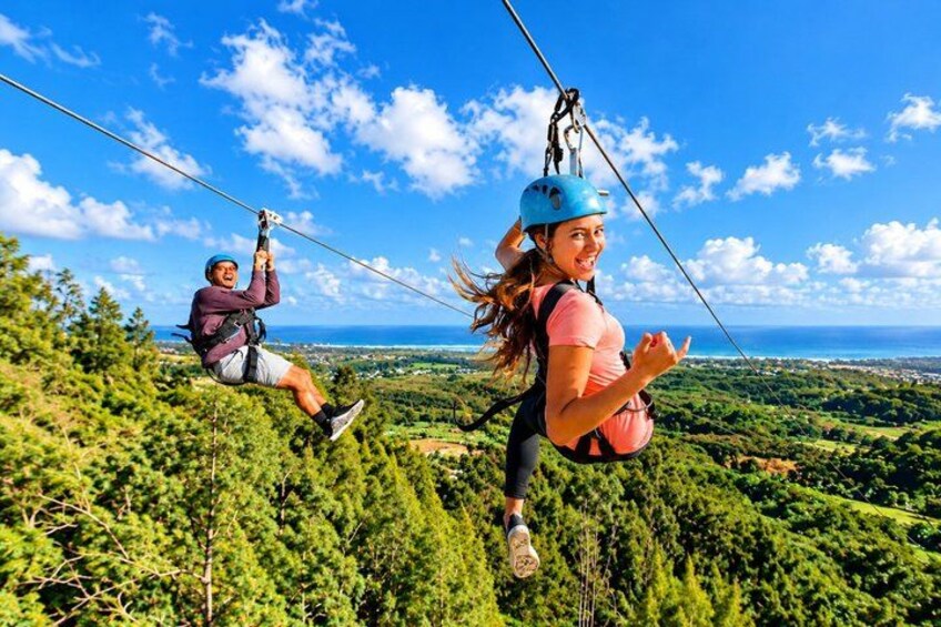 Two people ziplining over a lush green landscape with a clear blue sky. 1