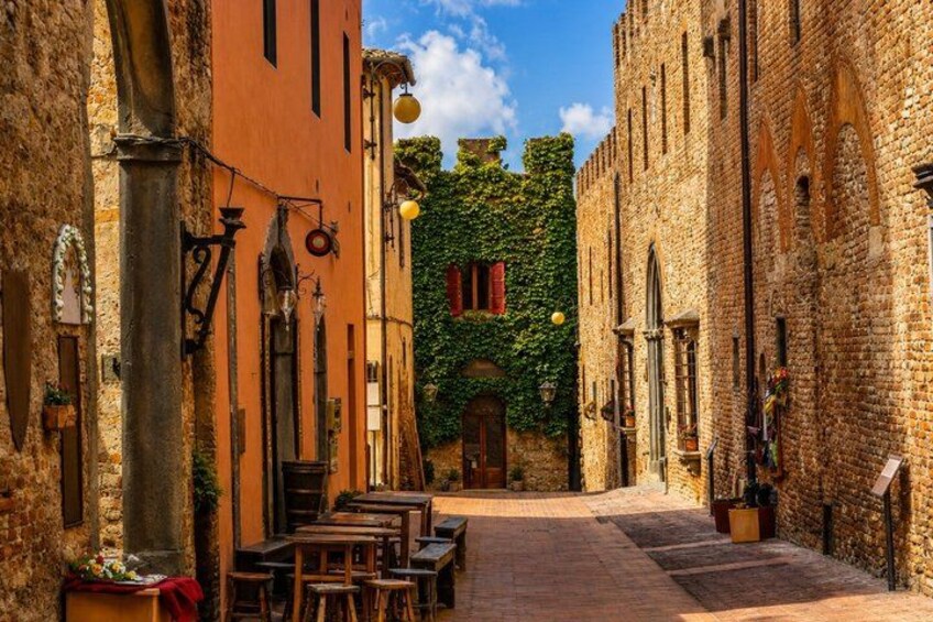 A narrow street with cobblestone pavement, rustic buildings, and a brick wall with greenery. 1