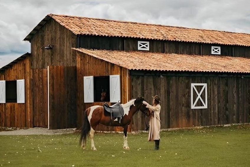 A wooden barn with a red roof, a horse with a saddle, and a person grooming the horse. 3