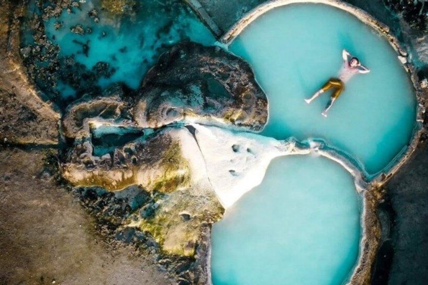 A person floating in a turquoise pool surrounded by rocky terrain. 1
