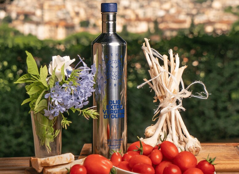 Une bouteille d’huile d’olive extra vierge, une tête d’ail, des tomates et un bouquet de fleurs sur une table en bois, avec un jardin flou en arrière-plan. 1