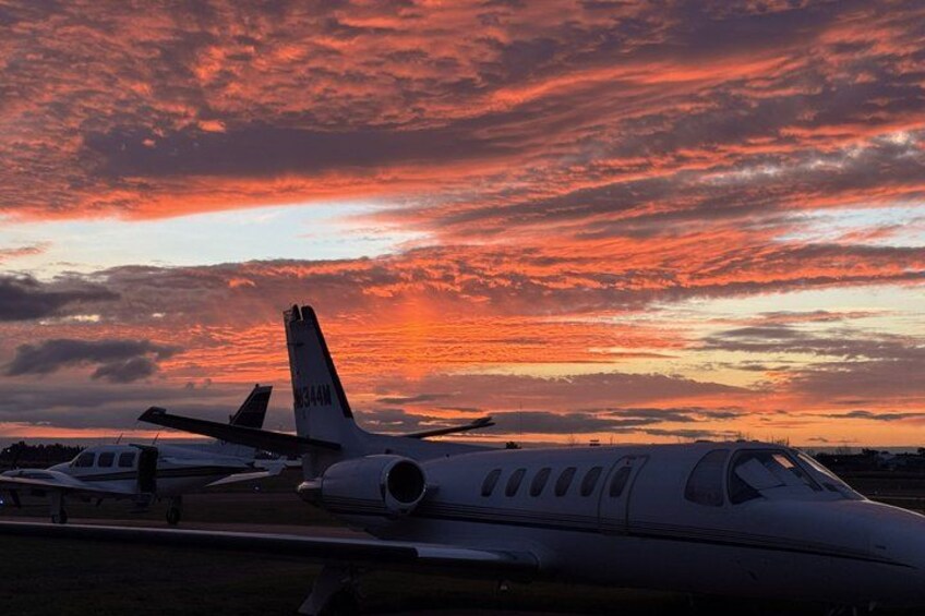 A private jet parked on a runway with a sunset in the background. 4
