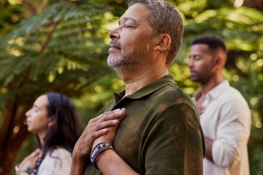 A person in a green shirt with a bracelet, standing outdoors with trees in the background. 1
