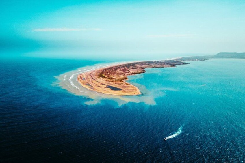 An aerial view of a coastal area with a curved shoreline, a small island, and a boat in the water. 3