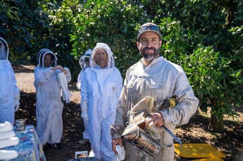 People in protective suits in an orchard, holding tools and containers. 1