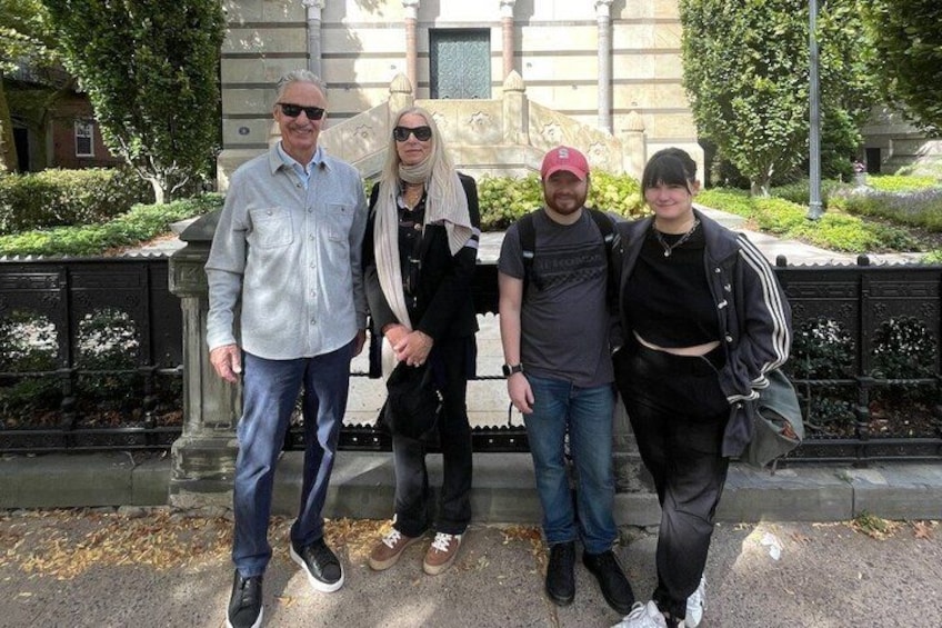 Four people standing in front of a stone structure with greenery in the background. 2