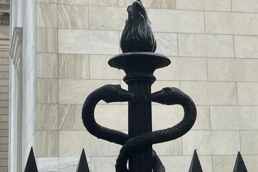 A black metal sculpture with a bird perched on top, two snakes entwined around a central column, and pointed spikes at the base. 5