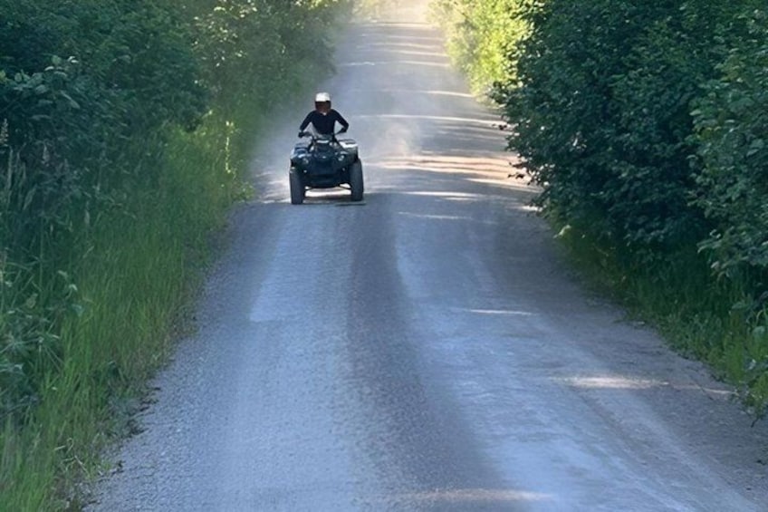 A person riding a quad bike on a narrow road surrounded by greenery. 3