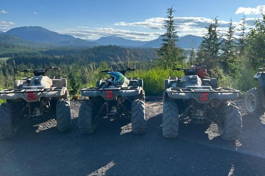 Four ATVs parked on a gravel road with a mountainous landscape in the background. 1