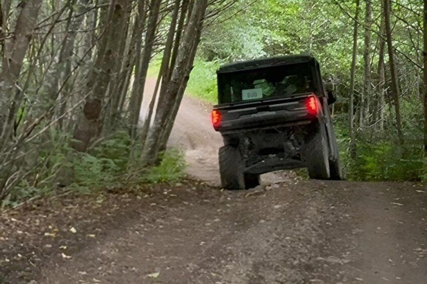 A vehicle driving on a dirt road in a forested area. 2