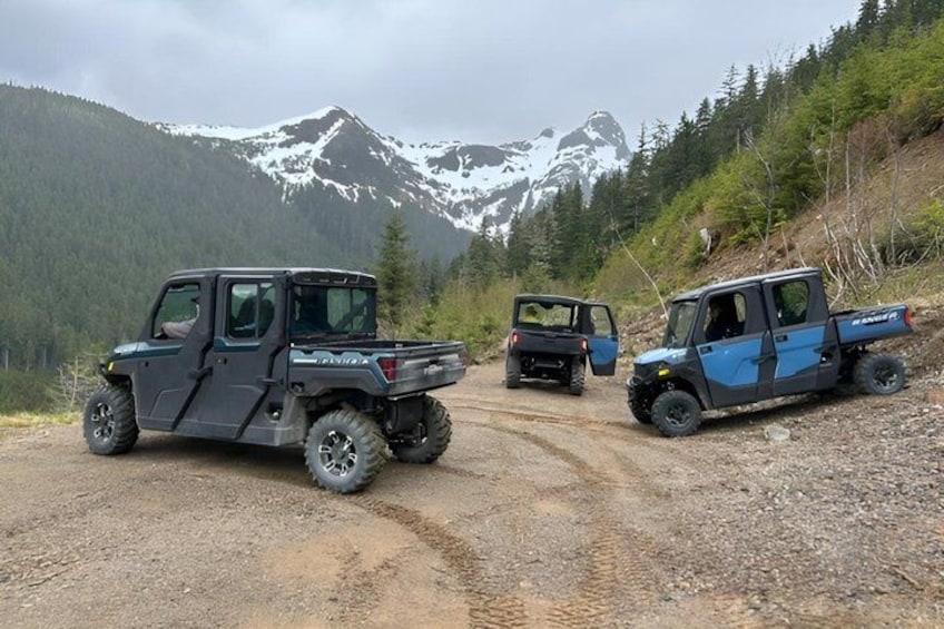 Three off-road vehicles parked on a dirt road with snow-capped mountains in the background. 4