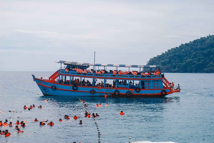A blue and red boat with people wearing life jackets on the water. 4