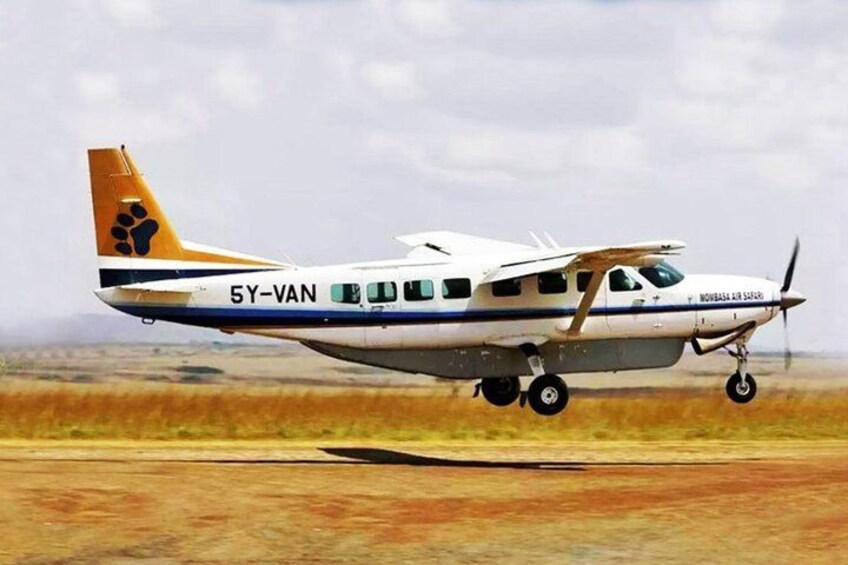 A small propeller plane with the registration number 5Y-VAN, flying over a flat landscape with sparse vegetation. 1