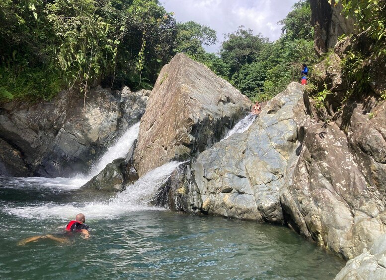 A waterfall in a rocky gorge with a person swimming in the water. 4
