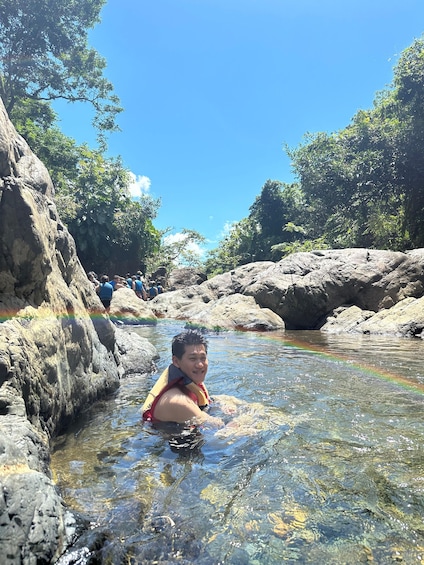A person in a rocky stream surrounded by large boulders and trees. 1