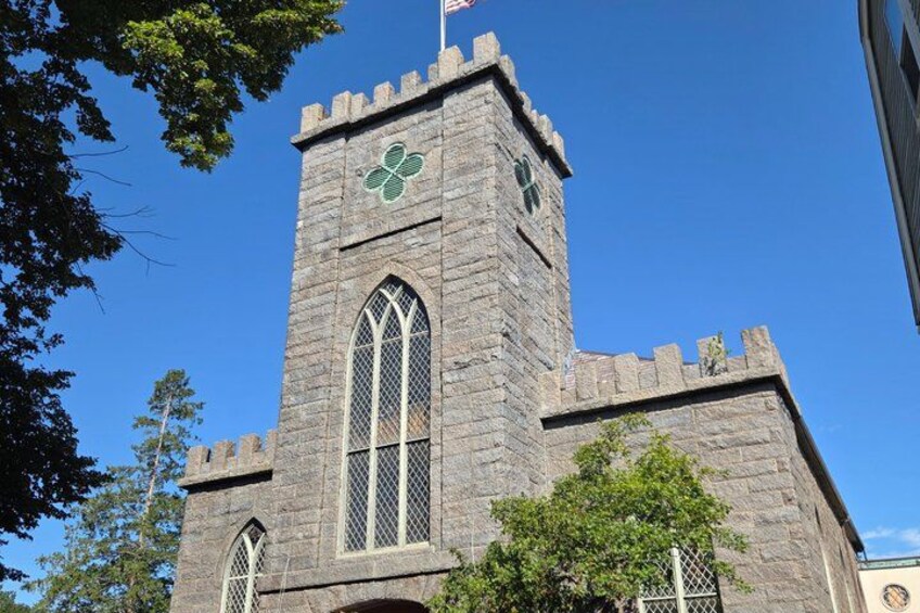 A stone church with a clock tower, a cross on the tower, and a flag. 2