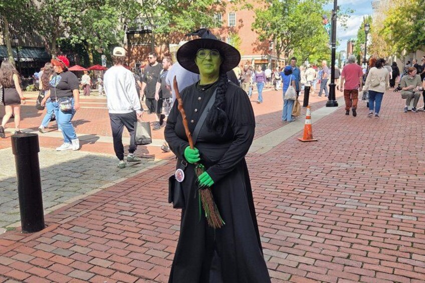 A person in a black costume with a green face, holding a staff, standing on a brick pavement. 3