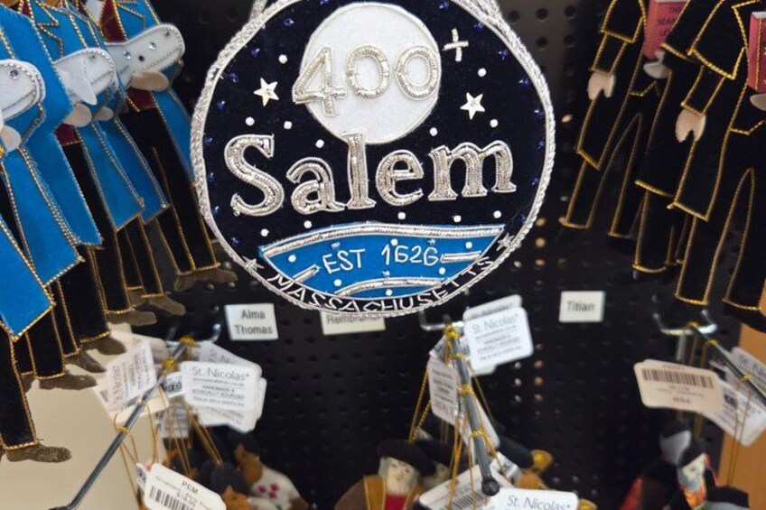 A circular sign with '400 Salem' and 'EST 1626' text, surrounded by various items like dolls and tags. 5