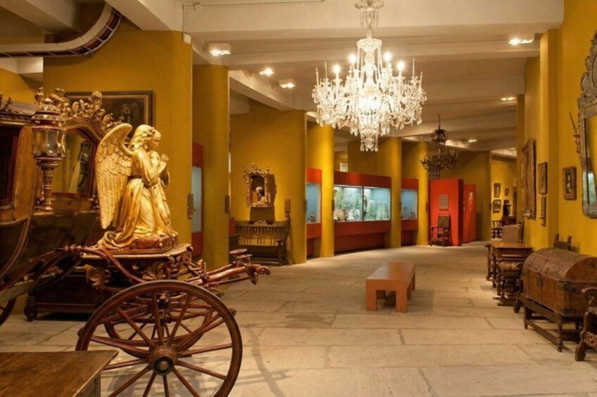 A grand hall with a golden statue, a chandelier, and a carriage. 3