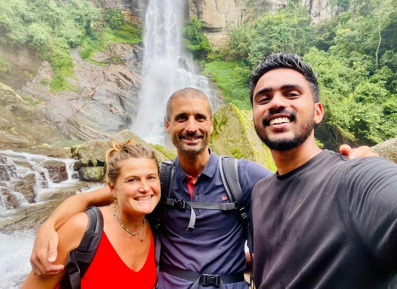 Three people taking a selfie in front of a waterfall surrounded by greenery. 1