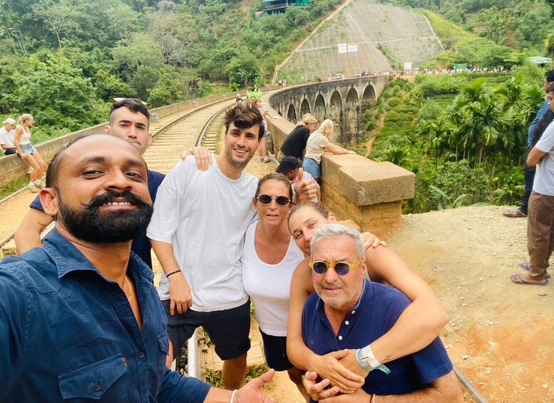 A group of people standing on a stone bridge with a railway track in the background. 2