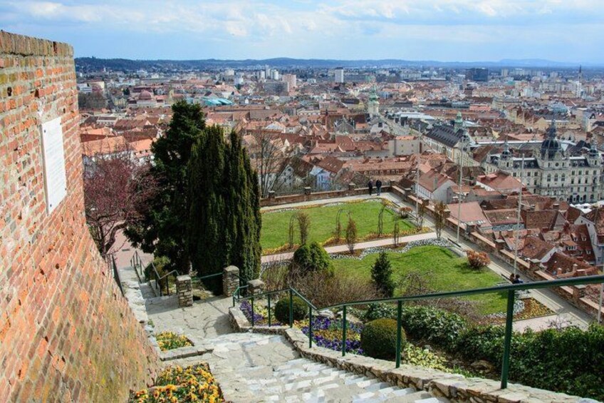A cityscape with a prominent brick wall, a grassy area with flowers, and a distant view of the city. 5