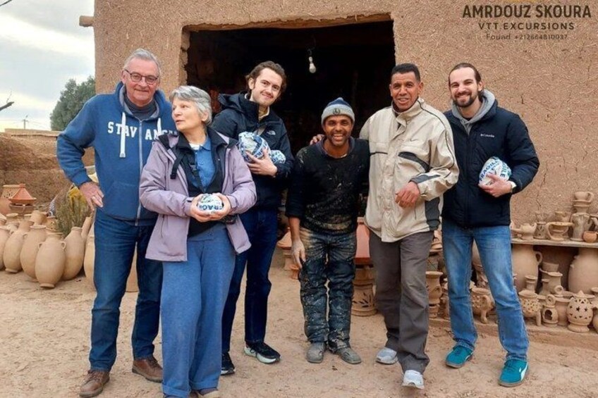 A group of people standing in front of a pottery workshop with clay pots and pottery wheels. 1