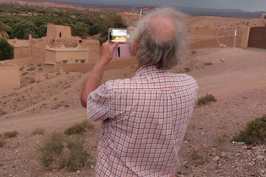 A man taking a photo of a desert landscape with buildings in the background. 3