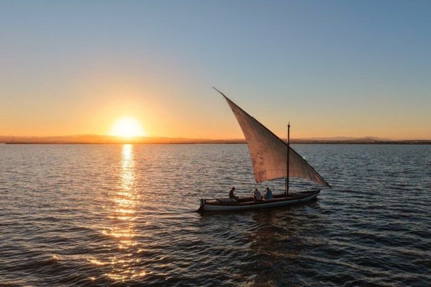 A sailboat with a single sail on calm water during sunset. 1