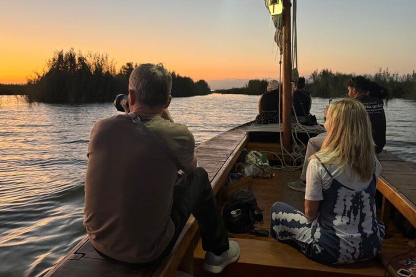 A sunset over a calm body of water with people on a boat. 4