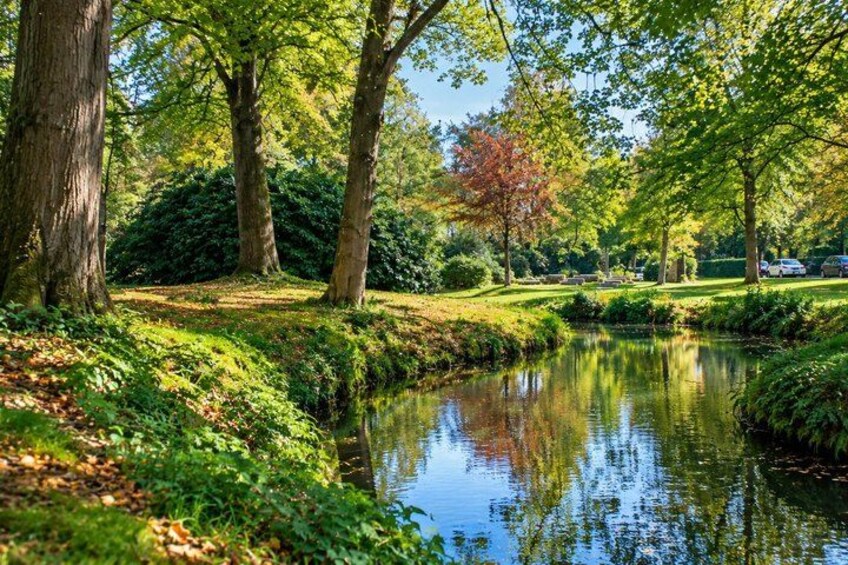 A serene park with a calm river, lush greenery, and tall trees. 2